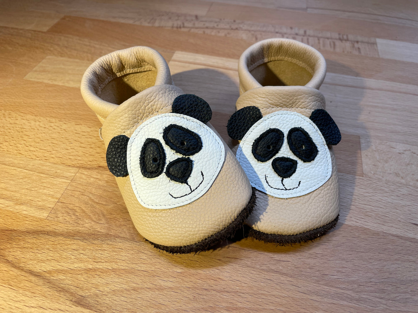 Cremefarbene Lederpuschen mit einem Pandabären